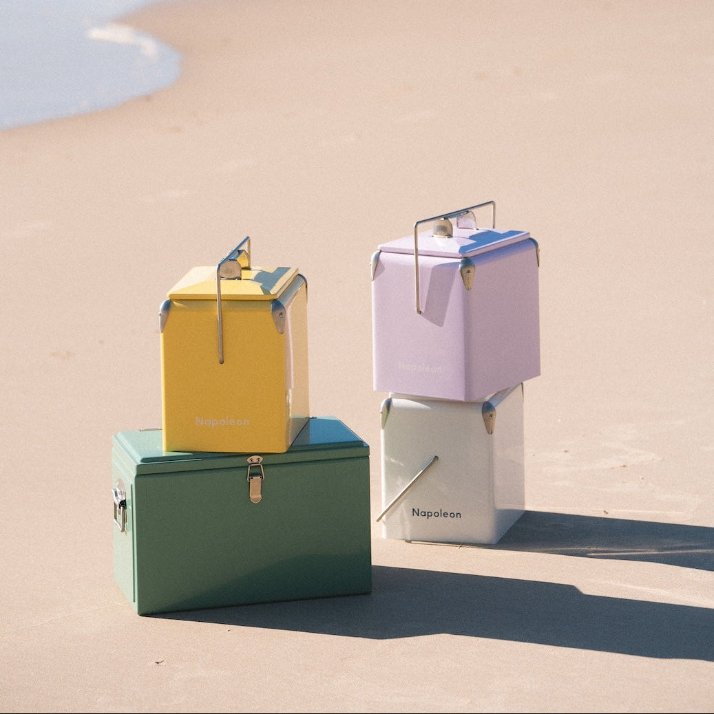Three colorful cooler stacked on a sandy surface with a blue sky.